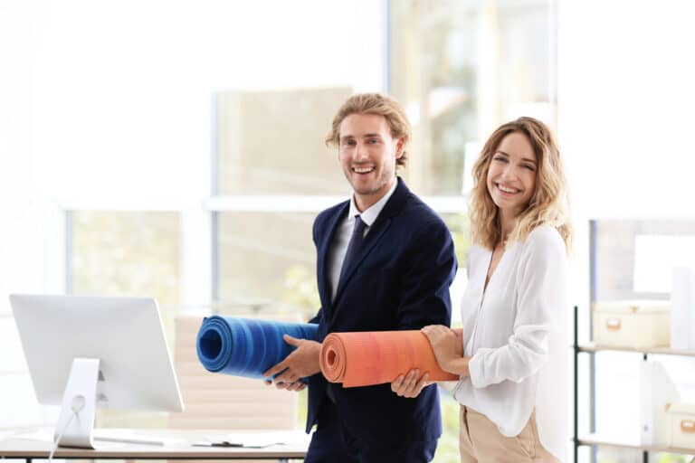 Collègues souriants en tenue de bureau tenant des tapis de yoga, illustrant le bien-être au travail en entreprise.